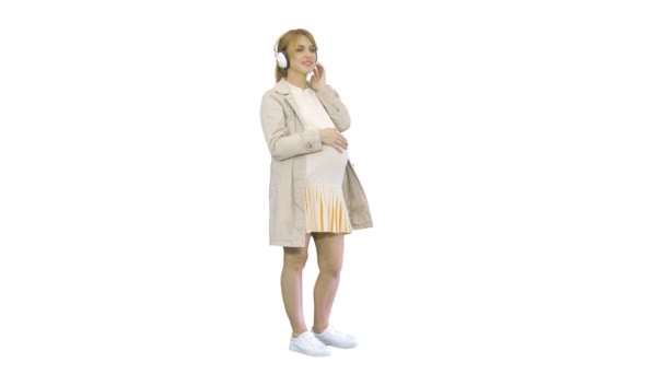 Mladý atraktivní těhotná žena poslech hudby ve sluchátkách na bílém pozadí. — Stock video