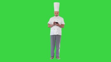 Beyaz üniformalı olgun bir aşçı yeşil ekranda, Chroma Key 'de cep telefonuna mesaj atıyor..