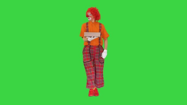 Clown draagt een geschenkdoos en kijkt erin op een groen scherm, Chroma Key. — Stockvideo