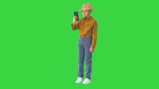 Petit garçon dans un chapeau de paille montrant autour tout en ayant un appel vidéo au téléphone sur un écran vert, Chroma Key. — Video