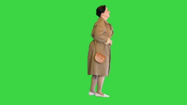 Dicke brünette Frau im Trenchcoat, die auf einem Green Screen läuft, Chroma Key. — Stockvideo