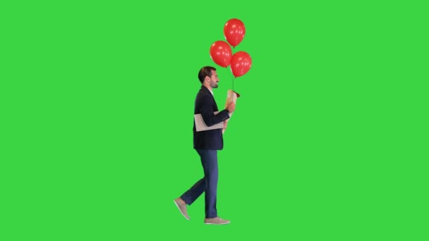 Elegancki mężczyzna, w garniturze, z bukietem kwiatów, prezentem i balonami spacerującymi po zielonym ekranie, Klucz Chroma. — Wideo stockowe