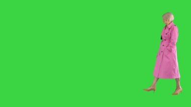 Pembe montlu son sınıf güzeli içeri girer ve yeşil ekran Chroma Key 'de kıyafetlerini kameraya gösterir..