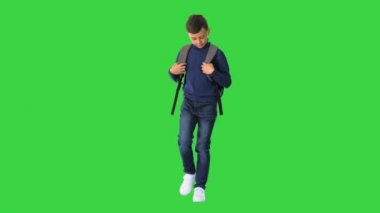 Polo yakalı neşeli bir çocuk yeşil ekranda sırt çantasıyla yürüyor, Chroma Key.