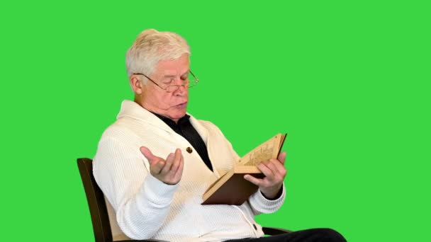 老人は、グリーンスクリーン、クロマキー上のカメラの本を声に出して読む. — ストック動画