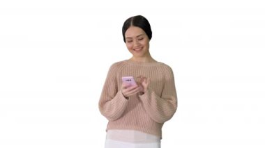 Gülümseyen genç bir kadın cep telefonuyla mesajlaşıyor ve beyaz arka planda gülüyor..