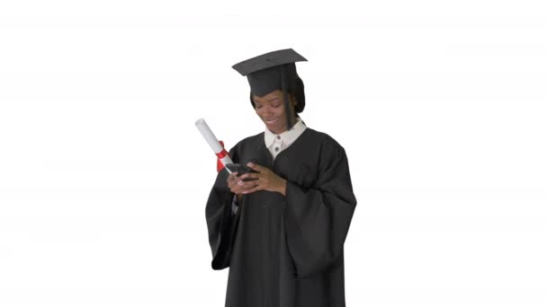 Glückliche afroamerikanische Absolventin mit Diplom und SMS auf ihrem Handy auf weißem Hintergrund. — Stockvideo
