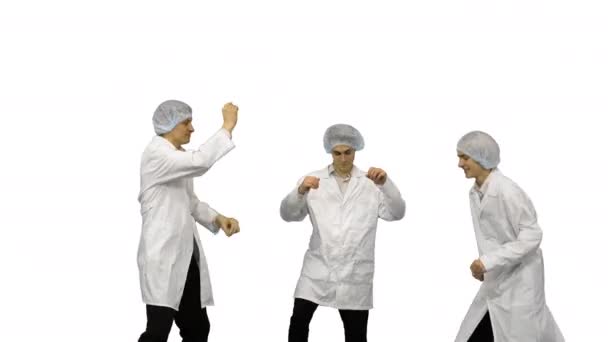 Tre manliga läkare i vita morgonrockar och skyddshattar gör roliga fest dans på vit bakgrund. — Stockvideo