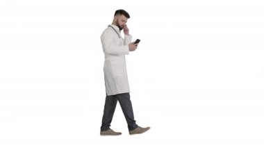 Beyaz üniformalı erkek doktor beyaz arka planda yürüyüp akıllı telefon kullanıyor..