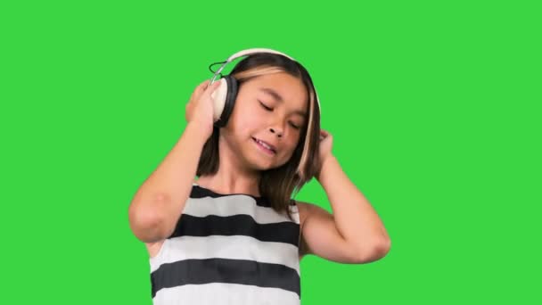 Gyönyörű aranyos boldog kislány fülhallgatóval zenét hallgatni a zöld képernyőn, Chroma Key. — Stock videók