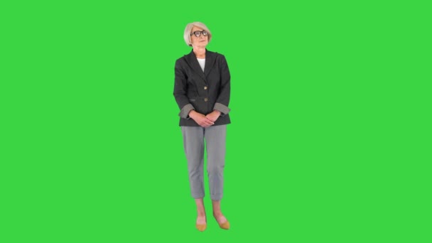 Чарівна літня жінка в модних окулярах стоїть і чекає на зеленому екрані, Хрома Кей.. — стокове відео