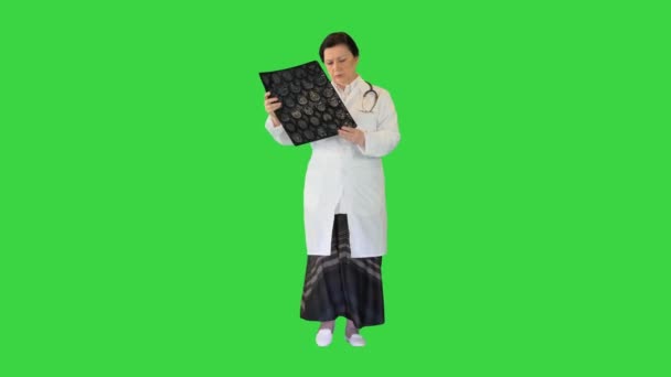 Dojrzała specjalistka sprawdzająca wyniki tomografii mózgu podczas chodzenia po zielonym ekranie, Chroma Key. — Wideo stockowe