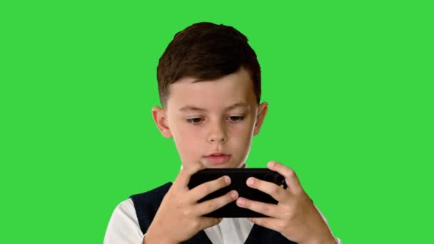 Koncentrerad pojke i väst med röstkommando för att titta på något på sin telefon på en grön skärm, Chroma Key. — Stockvideo