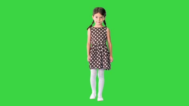 身着波尔卡圆点裙的小女孩穿着猪尾巴走路，在绿色屏幕上害羞地对着摄像机笑，铬钥匙. — 图库视频影像