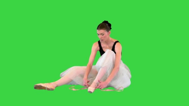 Ballerina veters up pointe met ballet linten tijdens het zitten op de vloer op een groen scherm, Chroma Key. — Stockvideo