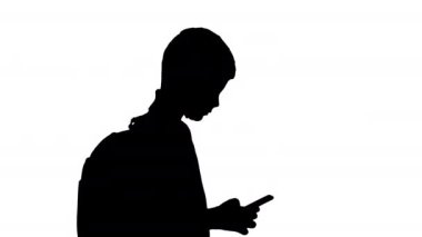 Sırt çantalı siluet öğrencisi yürürken cep telefonundan mesaj atıyor..