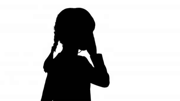 Silhouette Nettes Mädchen in Weiß mit Kopfhörern in der einen Hand und Kopfnicken zur Musik beim Gehen. — Stockvideo