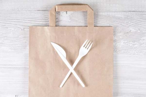 Stop using plastic. Plastic waste concept. Close up. Brown ecological paper bag and crossed plastic forks and knife on it. Concept of Recycling plastic and ecology problem.