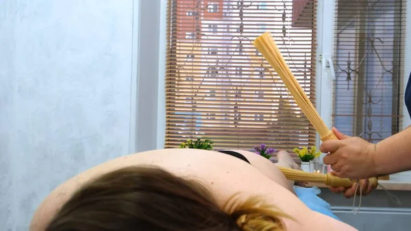 De masseur maakt anti-cellulitis massage van vet vrouwelijke benen met bamboe stokken. De therapeut maakt behandelingen om de conditie van de huid te verbeteren. Agressieve strijd tegen vet. Kuuroord. — Stockfoto