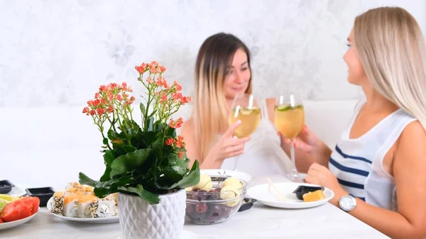 Two attractive girls, cheerful best friends having fun and drinking wine at home. Two glasses of white wine in hands. Girls having fun time together gossiping. — Stock Photo, Image