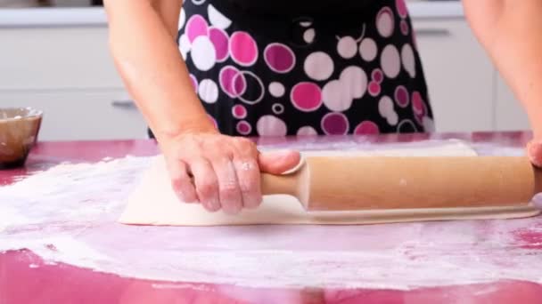 Kobiece dłonie zwijają ciasto wałkiem na drewnianej powierzchni, z bliska. kobiece ręce toczące ciasto na liliowym stole. Ręce szefa kuchni głaskają ciasto. Ręce rozwałkować ciasto z toczenia — Wideo stockowe