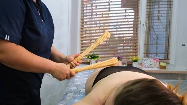 Le masseur fait un massage anti-cellulite des grosses jambes féminines avec des bâtons de bambou. Le thérapeute fait des traitements pour améliorer l'état de la peau. Lutte agressive contre la graisse. Traitement spa. — Photo