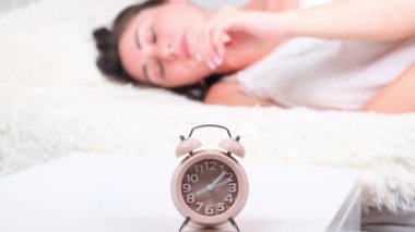 Yataktaki kadın sabah çalar saati kapatıyor. Kadın erken kalkmak istemiyormuş. Alarm saati yakın plan.