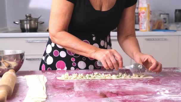 Vrouwelijke handen leggen de vulling op het deeg. Lekkere krullende broodjes maken, khachpuri met kaas — Stockvideo