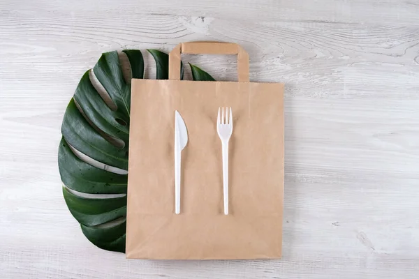 Plastikgabel, Messer auf Papiertüte. Umweltfreundliche Lebensmittelverpackungen und umweltfreundliche Baumwolltaschen auf grauem Hintergrund mit Kopierraum. Pflege der Natur und Recyclingkonzept. Container für Catering und Straßenfasten — Stockfoto