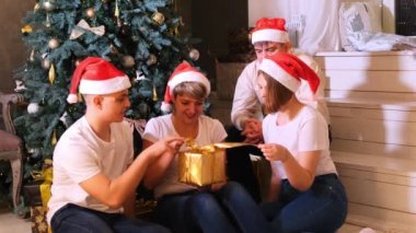 Noel şapkalı aile Noel ağacının önünde hediyelerini değiş tokuş ediyor..