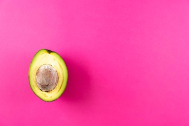 Pembe arka planda yarım taze avokado meyvesi