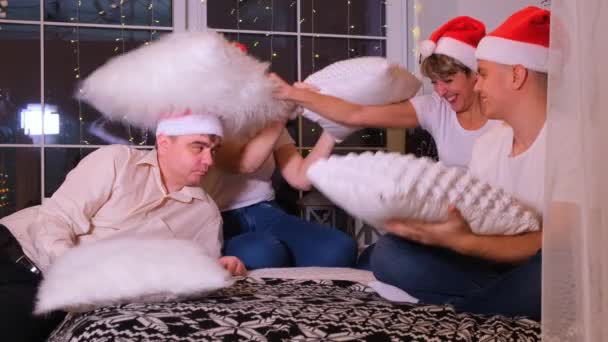 Szczęśliwa rodzina w Boże Narodzenie kapelusze zabawy i walki poduszki na łóżku. — Wideo stockowe