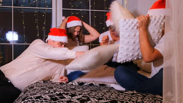 幸せなクリスマスの帽子の家族はベッドで枕を楽しんで戦っています. — ストック写真