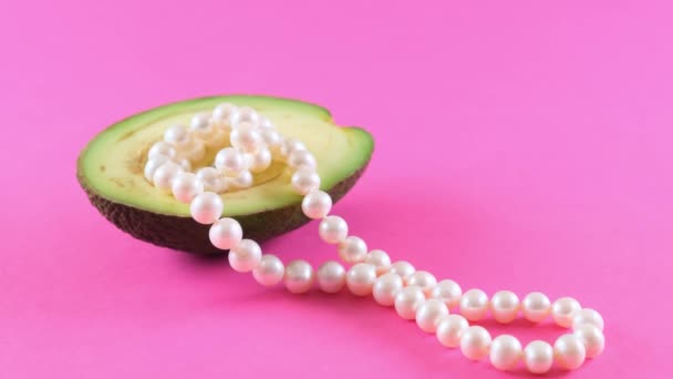 Напівсвіжі фрукти авокадо з перлами на рожевому фоні. Модний дизайн продуктів харчування . — стокове відео
