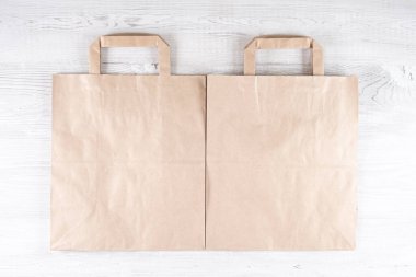 Beyaz ahşap bir masada iki kahverengi ekolojik kese kağıdı. Logonuz için yer.