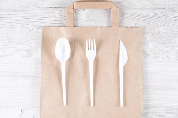 plastic fork, spoon, knife on paper bag. Eco-friendly food packaging and cotton eco bags on gray background with copy space. Carering of nature and recycling concept. containers for catering and