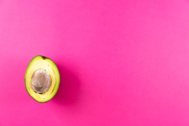 Pembe arka planda yarım taze avokado meyvesi