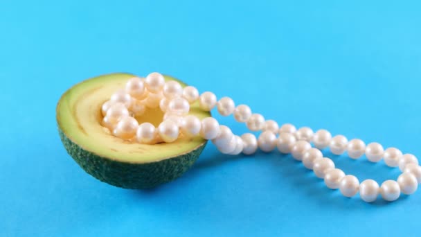 Napůl čerstvé avokádové ovoce s perlami na modrém pozadí. Módní design potravin. — Stock video