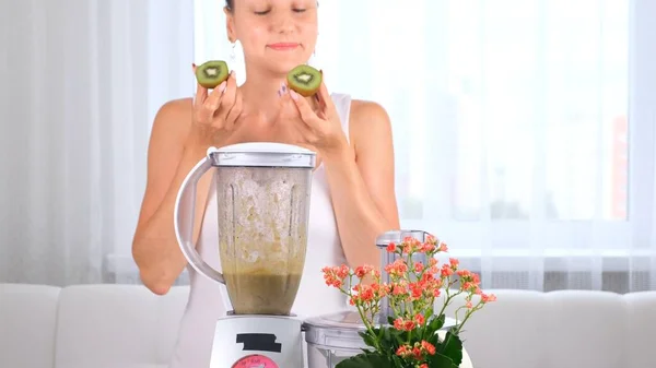 Glückliche junge Frau bereitet köstlichen nahrhaften Smoothie im Kiwi-Mixer zu — Stockfoto