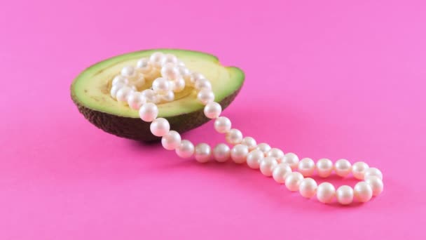 Half vers avocado fruit met parels op een roze achtergrond. Modieus voedselontwerp. — Stockvideo