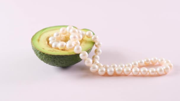 Mezzo avocado con perle su fondo rosa chiaro. surrealismo. Design alimentare alla moda. — Video Stock