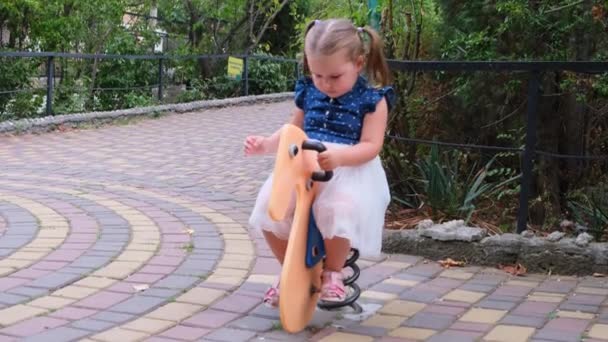 Niña pequeña juega y rueda en un columpio en un parque infantil — Vídeo de stock