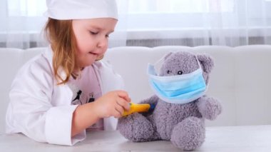Küçük kız doktorculuk oynuyor, sıcaklığı ölçüyor. Mutlu çocuk küçük doktor bir oyuncak ayıyı muayene ediyor.