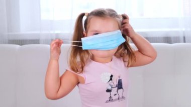 Küçük kız koronavirüs ve çeşitli enfeksiyonlara karşı koruyucu bir maske takıyor. Karantina, hastalık. Kız koruyucu maskesini çıkarıyor ve salgının sonunda seviniyor.
