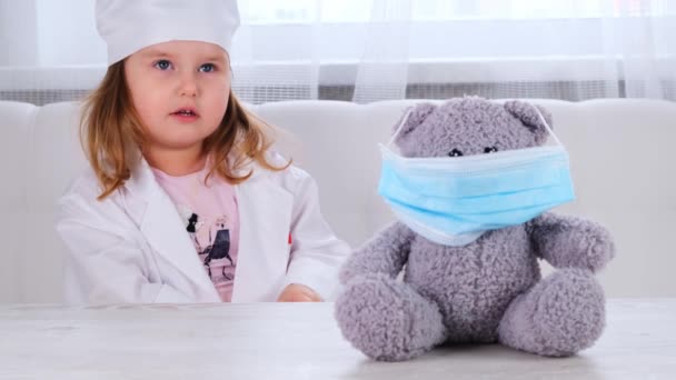Petite fille joue un médecin, fait une injection. Enfant heureux petit médecin examine un ours en peluche. Concept de traitement par le virus Corona, injection pendant une pandémie — Video