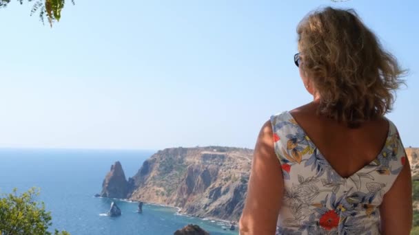 Mulher admira uma bela vista da costa do mar azul-turquesa e montanhas no Cabo Fiolent, Crimeia. — Vídeo de Stock