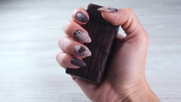 Vrouwelijke hand met mooie manicure nagels in de vorm van chocolade snoepjes, met een ongewalste reep pure chocolade, close-up. Geniet van het dessert. — Stockvideo