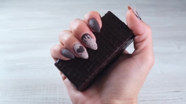 Vrouwelijke hand met mooie manicure nagels in de vorm van chocolade snoepjes, met een ongewalste reep pure chocolade, close-up. Geniet van het dessert. — Stockvideo