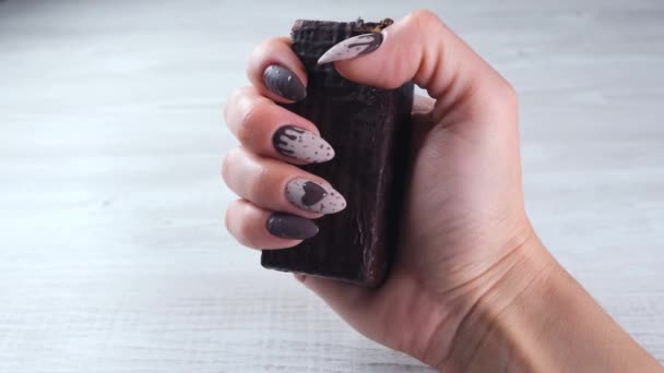 Vrouwelijke hand met mooie manicure nagels in de vorm van chocolade snoepjes, met een ongewalste reep pure chocolade, close-up. Geniet van het dessert. — Stockvideo