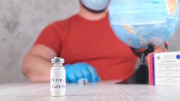 Lahvička s vakcínou proti koronaviru, na pozadí člověk očkuje planetu, zeměkouli. Koncepce léčby koronového viru, injekce během pandemie. Cestovní koncept během pandemie — Stock video